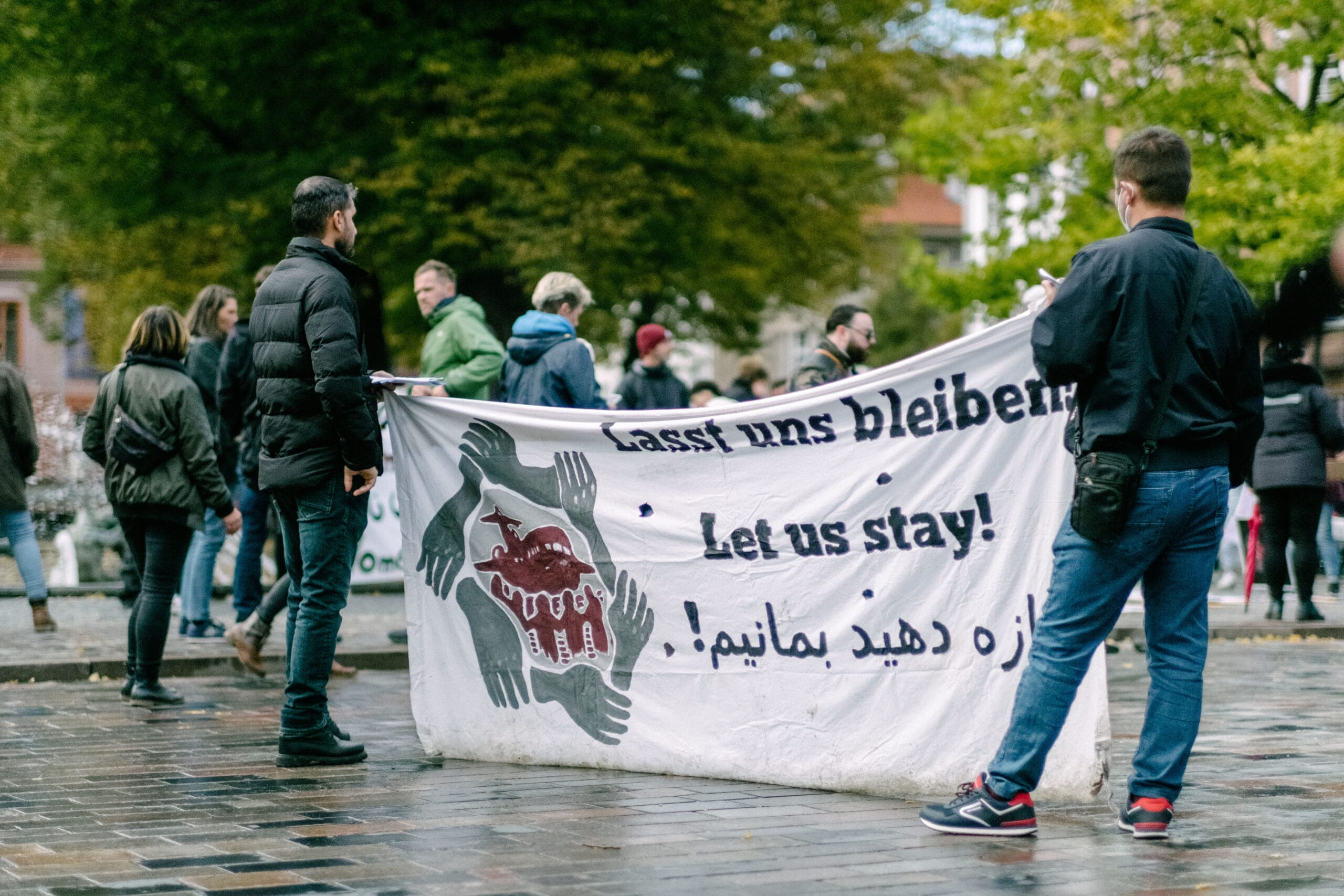 Zwei Personen halten ein großes Transparent mit der Aufschrift “Lasst uns bleiben!”