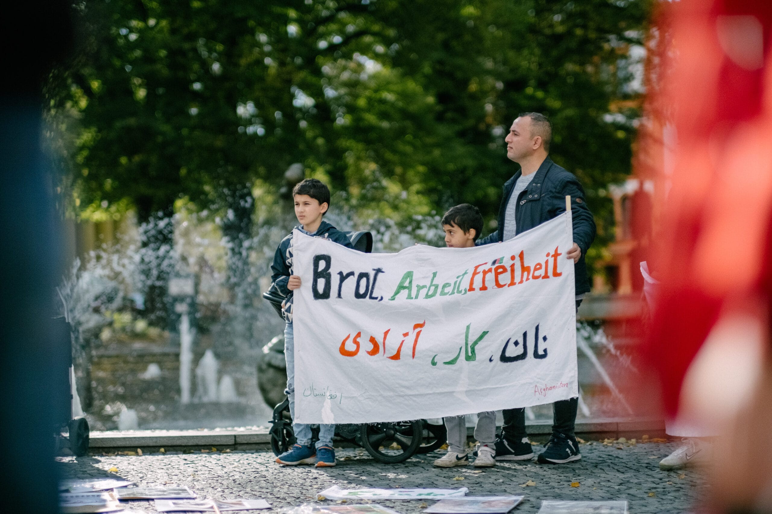 Ein Erwachsener und zwei Kinder halten ein Transparent mit der Aufschrift “Brot, Arbeit, Freiheit”. 