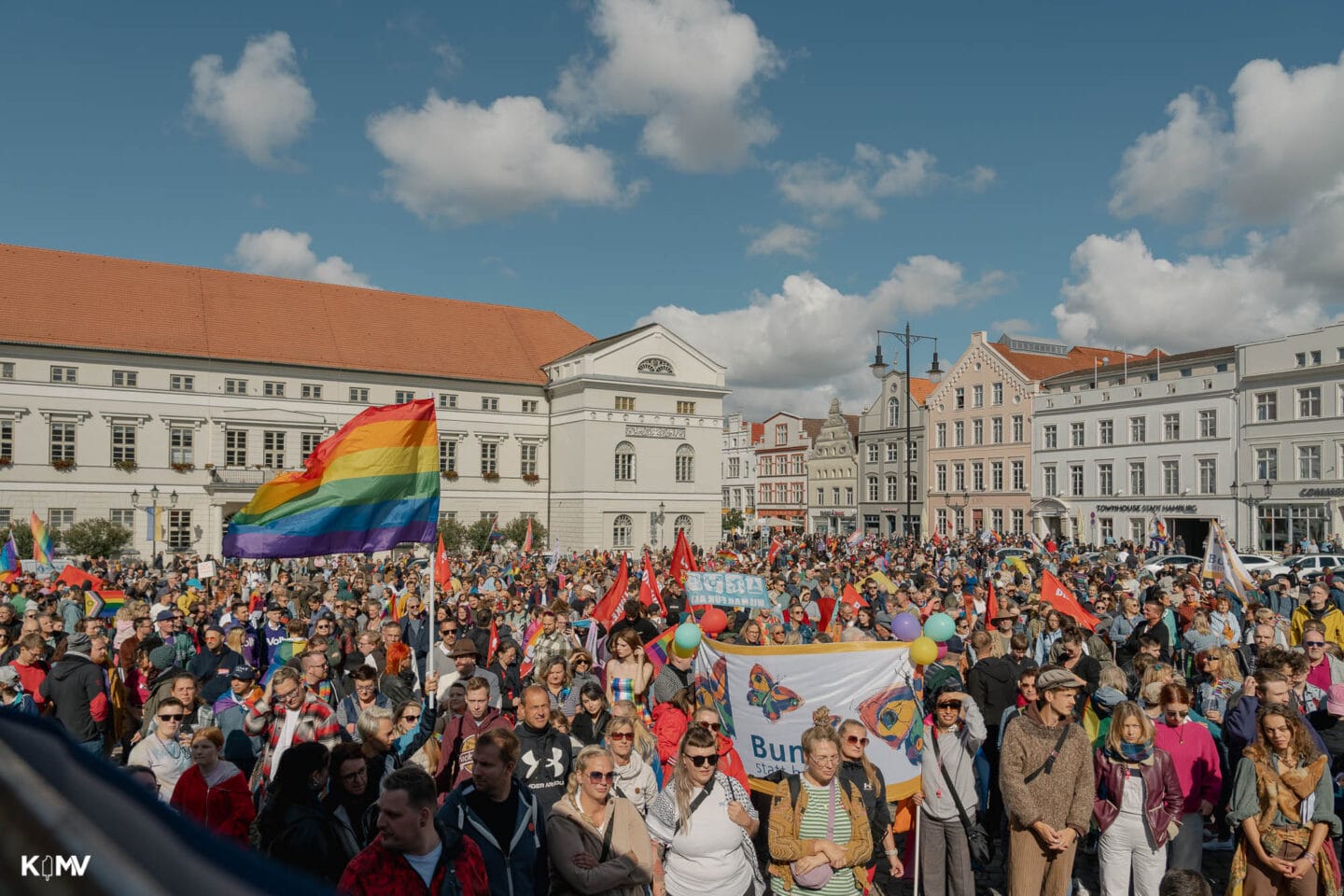 Der Marktplatz in Wismar war zu Beginn des CSD voll. Zahlreiche Demonstrierende hatten sich teilweise in bunten Kostümen, mit Flaggen oder Schildern versammelt.