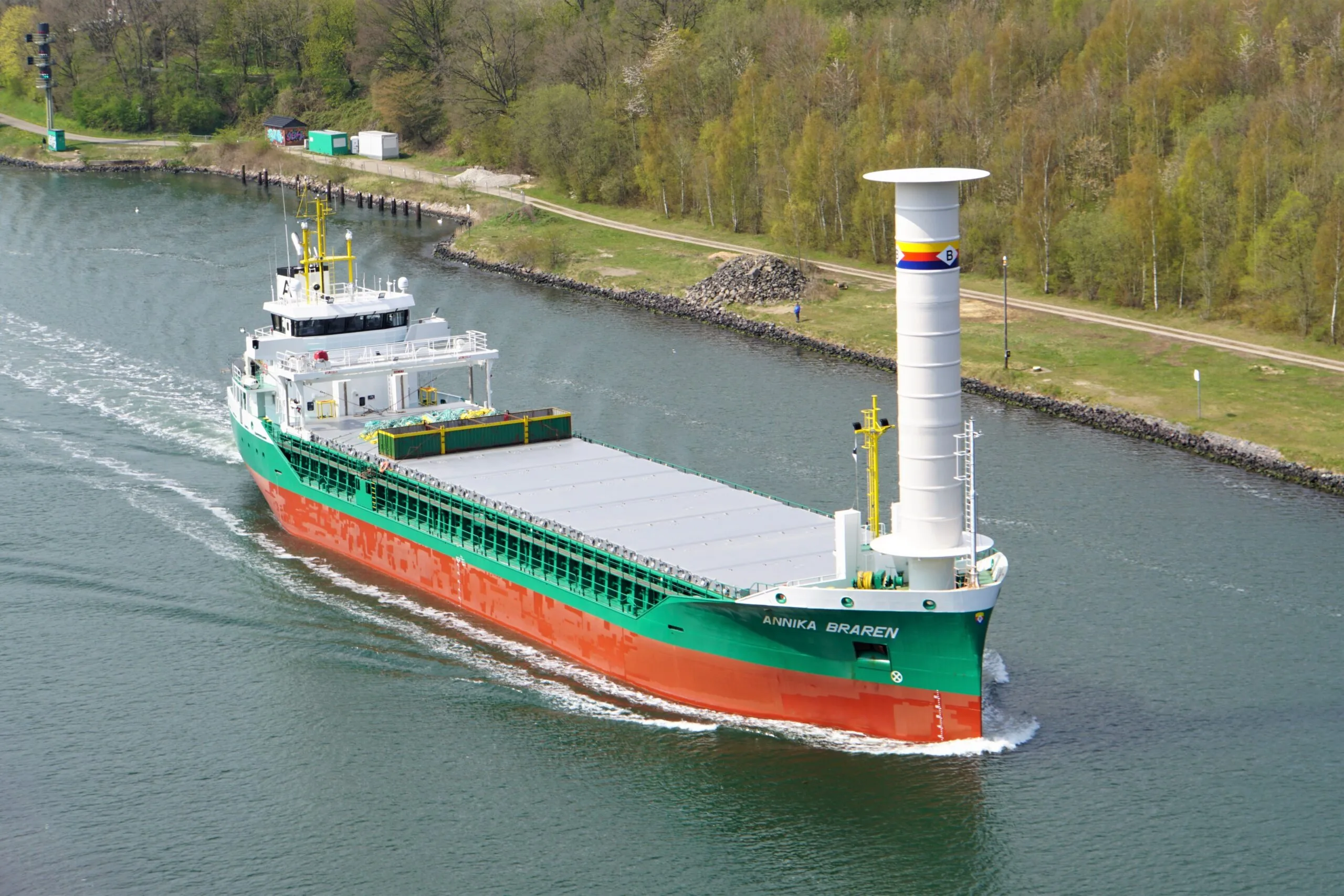 Containerschiff fährt in einem Kanal mit einem Flettner-Rotor im vorderen Schiffsbereich.