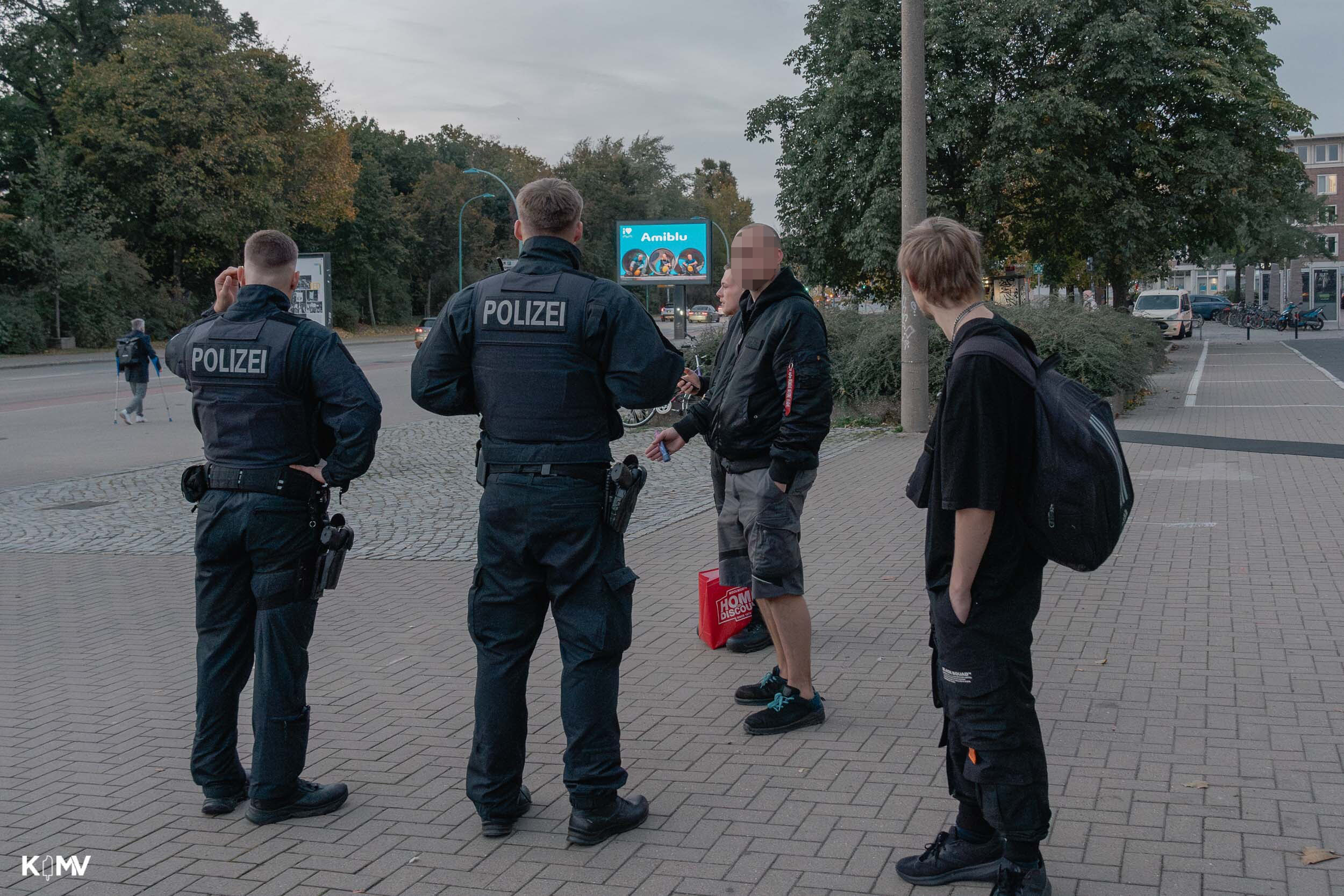 Zu sehen sind zwei Polizeibeamte, die mit einer Gruppe von Jugendlichen spricht. 