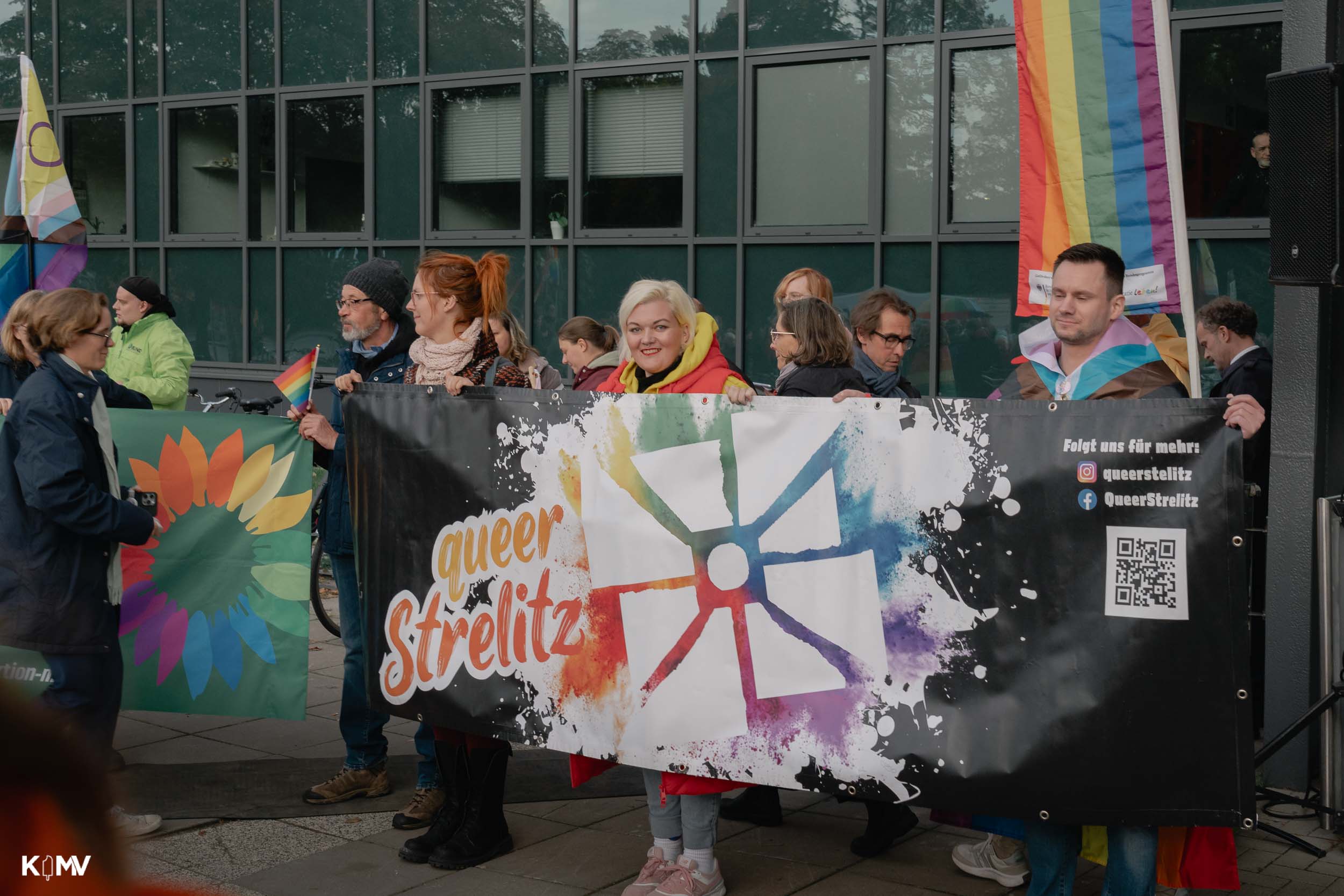 Mitglieder und Unterstützer:innen halten ein Plakat vom Verein „queerstrelitz“ hoch. 