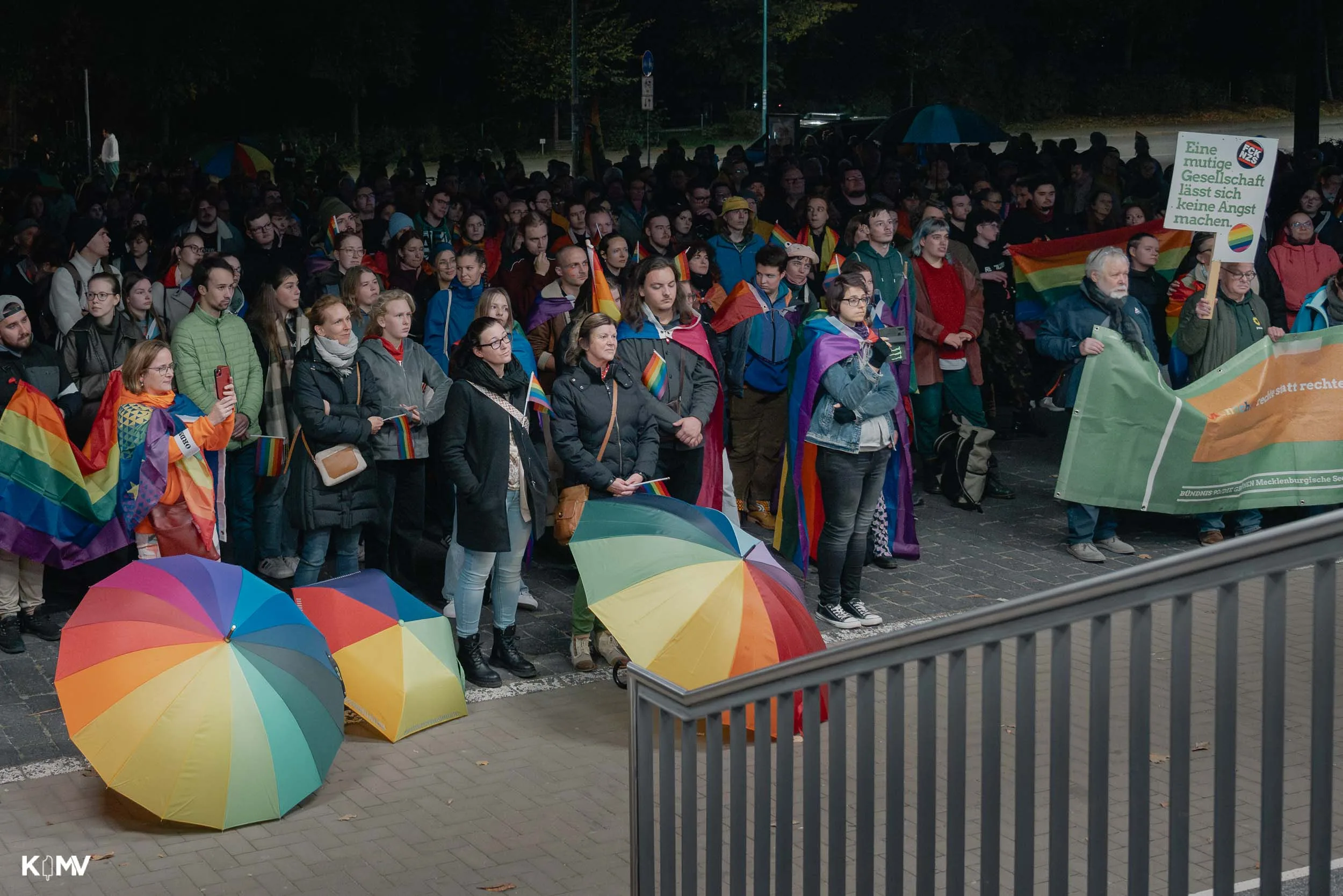 Es ist dunkel und noch immer steht eine große Menschenmenge mit Regenbogenflaggen und -schirmen vor dem Rathaus.