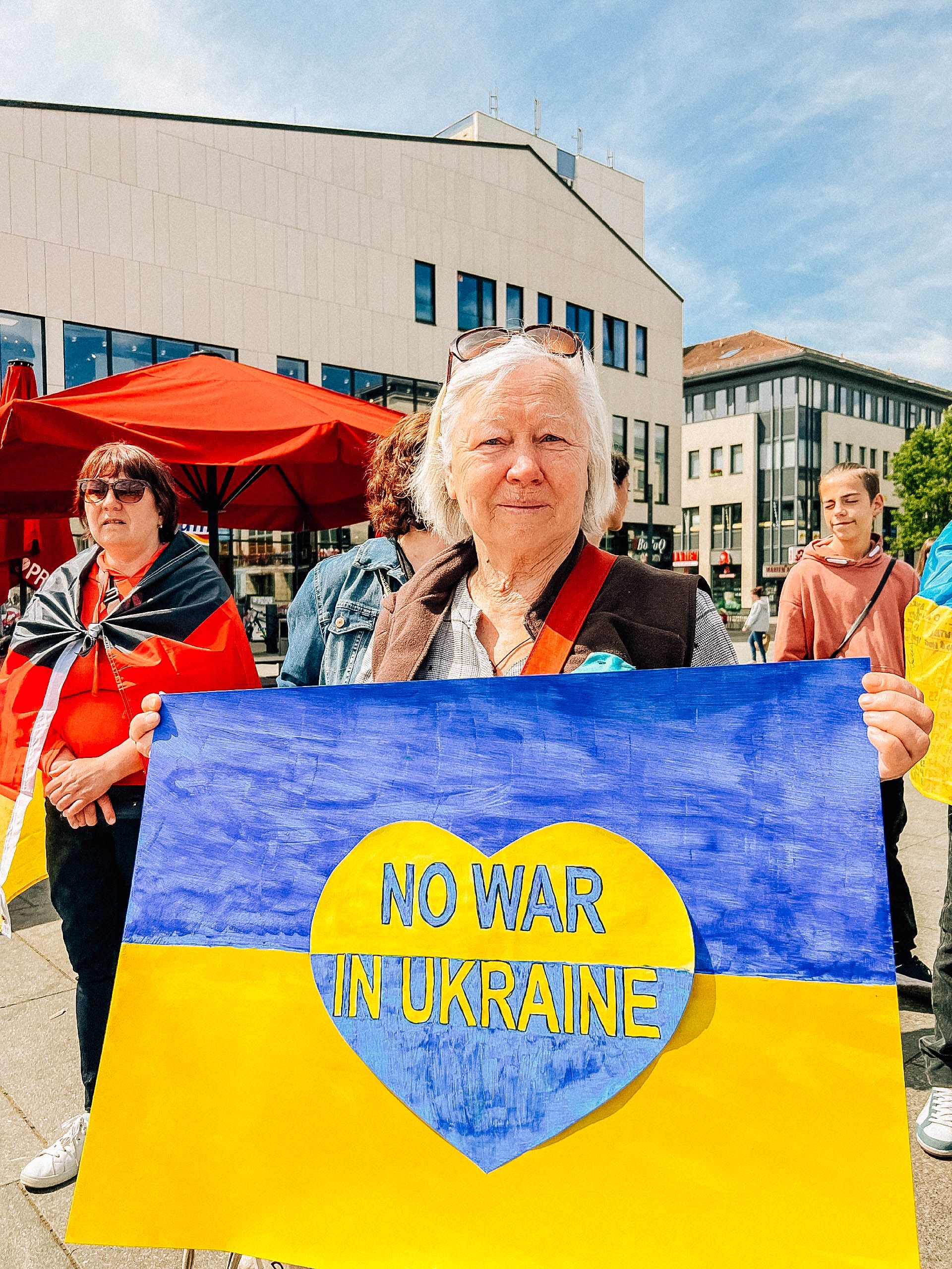 Foto; Eine Demonstration hält ein blau-gelbes Protestschild mit der Aufschrift 